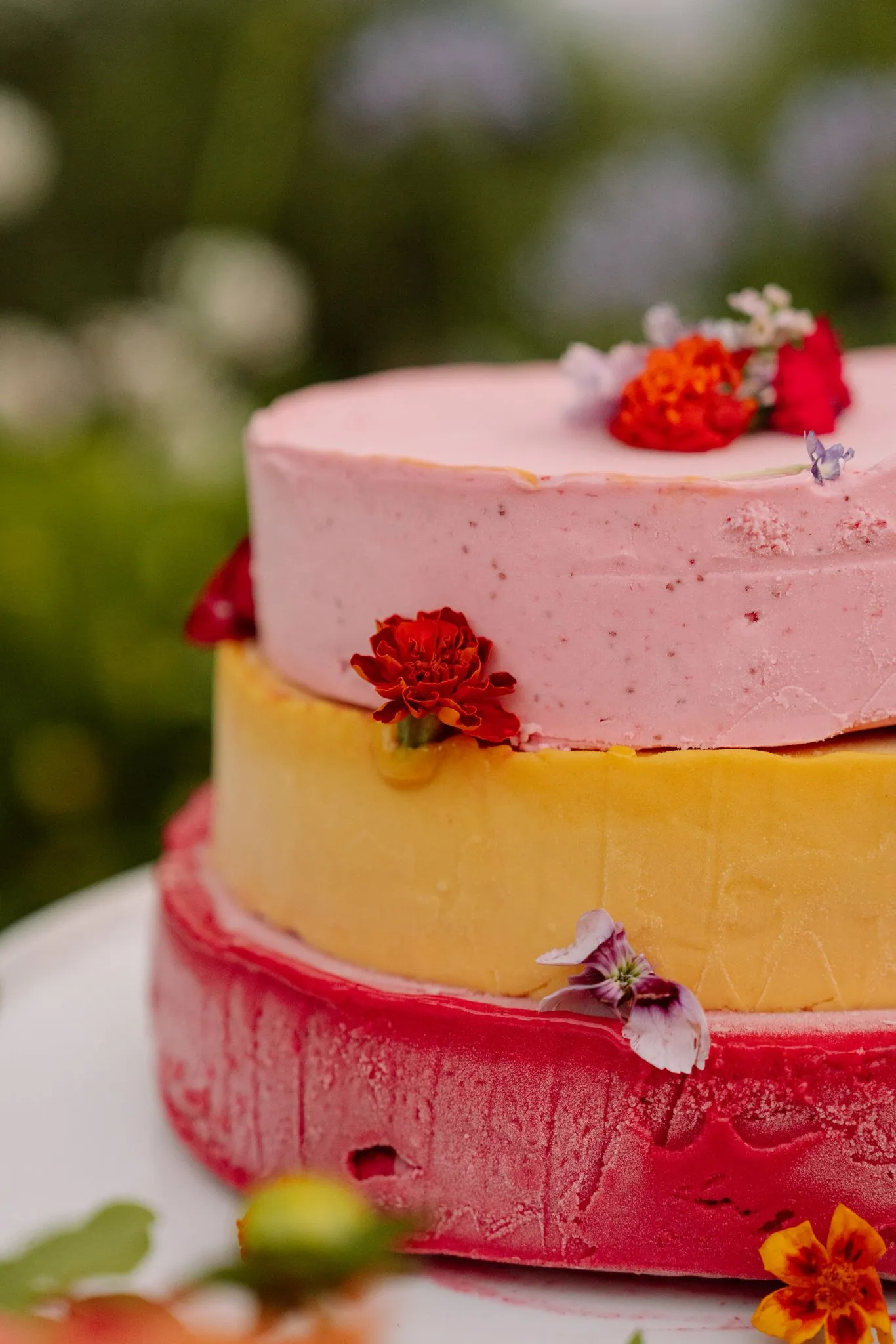 A three-tier celebration cake in pink, marigold and watermelon, dressed with edible flowers