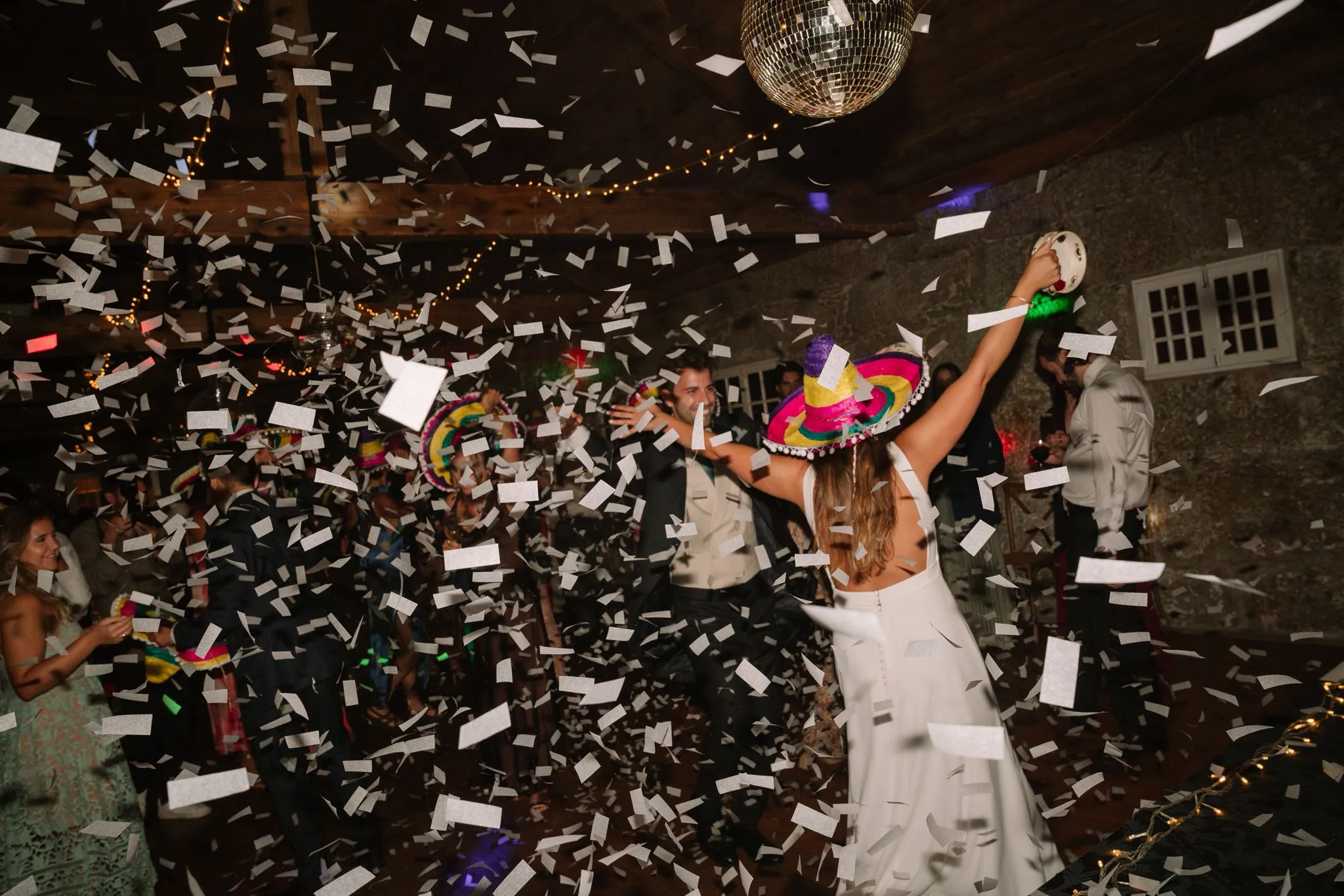 A bride throwing confetti under a mirror ball, wearing a bright sombrero